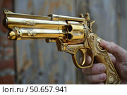 Hand holding golden gun with ornate engravings. Стоковое AI-изображение, AI-художник Иван Рябоконь / Фотобанк Лори