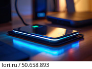 Smartphone charging wirelessly on induction charger at night. Стоковое AI-изображение, AI-художник Иван Рябоконь / Фотобанк Лори