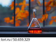Erlenmeyer flask containing orange liquid sitting on windowsill with autumn leaves background. Стоковое AI-изображение, AI-художник Иван Рябоконь / Фотобанк Лори