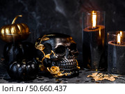 Halloween celebration. Black skull with golden roses, pumpkins, and black candles. Decor for the Day of the Dead or Halloween on a black background. Стоковое фото, фотограф Photojuli / Фотобанк Лори