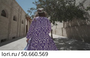 A young woman with long hair in an oriental robe and a skullcap walks through an ancient oriental city. Стоковое видео, видеограф Aleksey Kidisyuk / Фотобанк Лори