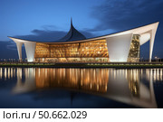 Nur sultan central concert hall reflecting on ishim river at twilight. Стоковое AI-изображение, AI-художник Иван Рябоконь / Фотобанк Лори