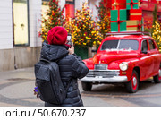 A girl blogger is filming Christmas-decorated streets. Gifts are delivered on the roof of a red Christmas retro car. Decorated New Year's Moscow. Стоковое фото, фотограф Photojuli / Фотобанк Лори