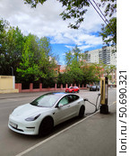 Белый электромобиль Tesla заряжается на улице (2024 год). Редакционное фото, фотограф Ирина Терентьева / Фотобанк Лори