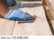 A carpenter wearing cloth gloves manually polishes wooden boards with sandpaper for grinding. The concept of DIY woodworking and construction. Стоковое фото, фотограф Photojuli / Фотобанк Лори