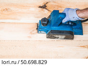 A hand-held electric planer in the hands of a craftsman. A man planing boards with an electric tool. Production of wooden products. Construction, wood processing. Стоковое фото, фотограф Photojuli / Фотобанк Лори