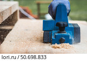A hand-held electric planer in the hands of a craftsman. A man planing boards with an electric tool. Production of wooden products. Construction, wood processing. Стоковое фото, фотограф Photojuli / Фотобанк Лори