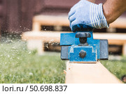 A hand-held electric planer in the hands of a craftsman. A man planing boards with an electric tool. Production of wooden products. Construction, wood processing. Стоковое фото, фотограф Photojuli / Фотобанк Лори