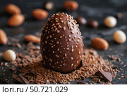 Delicious chocolate easter egg covered with hazelnut crumbles and chocolate shavings. Стоковое AI-изображение, AI-художник Иван Рябоконь / Фотобанк Лори