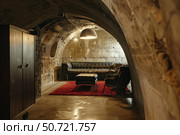 Modern underground bunker lounge with leather furniture and red rug. Стоковое AI-изображение, AI-художник Иван Рябоконь / Фотобанк Лори