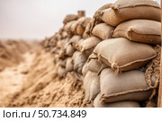 Sandbags line a protective barrier in a construction area during daytime. Стоковое AI-изображение, AI-художник Katsiaryna Repich / Фотобанк Лори