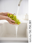 Close up view of a woman washes fresh green grapes under the pressure of flowing water in the white kitchen. Стоковое фото, фотограф Vladimir Drozdin / Фотобанк Лори
