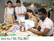 Multiethnic participants in coterie practice sewing, chatting, work textile and paper dress pattern. Стоковое фото, фотограф Яков Филимонов / Фотобанк Лори