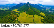 Aerial view of spectacular mountain range with green fields and forest in rural valley, amazing nature landscape for travel inspiration. Стоковое AI-изображение, AI-художник Павел Муравьев / Фотобанк Лори