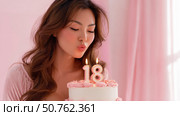 Young woman blowing out candles on an 18th birthday cake in a soft pink setting, celebrating adulthood with joy and elegance, captured in a warm, intimate close-up. Стоковое AI-изображение, AI-художник Катерина Бондарец / Фотобанк Лори