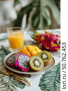 Colorful exotic fruits and juice on plate with tropical decor. Стоковое AI-изображение, AI-художник Катерина Бондарец / Фотобанк Лори