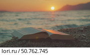 Open book rests on pebbles as sun sets over ocean in serene landscape of Croatia. Стоковое видео, видеограф Igor Tichonow / Фотобанк Лори