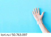 Human hand in transparent vinyl glove raised above light blue background. Safety and selfcare concept. Стоковое фото, фотограф Акимова Надежда / Фотобанк Лори