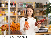 Teen girl hold packages bottles and choose consider juice in store. Стоковое фото, фотограф Яков Филимонов / Фотобанк Лори