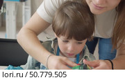 A caring young art teacher assists a boy in creating drawings on clothing during a master class. Стоковое видео, видеограф Strunov David / Фотобанк Лори