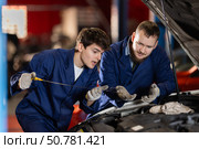 Two auto mechanics checking engine oil level under the hood of car together in garage. Стоковое фото, фотограф Яков Филимонов / Фотобанк Лори
