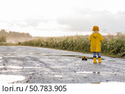 A boy in yellow rubber boots and a raincoat runs through puddles, having fun and playing with a remote-controlled car after it rains. Summer and autumn holidays. A happy childhood. Стоковое фото, фотограф Photojuli / Фотобанк Лори