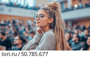 Thoughtful Woman with Dreadlocks in a Crowded Auditorium. Стоковое AI-изображение, AI-художник Данила Большаков / Фотобанк Лори