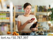 European young woman customer at shop scans QR code on pomegranate juice bottle using phone camera. Стоковое фото, фотограф Яков Филимонов / Фотобанк Лори