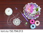 Crocheting lace napkin. Bouquet of flowers, crochet hooks, skeins of colored cotton yarn, pins on wooden table. DIY concept. Crochet as a hobby. Copy space, flat lay, close-up, top view. Стоковое фото, фотограф Виктория Катьянова / Фотобанк Лори