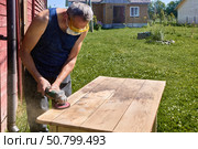 Sanding wood surface with power tool, DIYer using protective gear during backyard work in countryside setting under bright sunlight. Стоковое фото, фотограф Владимир Григорьев / Фотобанк Лори