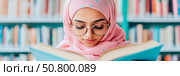 Concept: Serene Learning - Muslim Woman Engrossed in a Book in Library, Design for educational material, poster. Стоковое AI-изображение, AI-художник Данила Большаков / Фотобанк Лори
