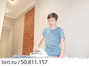 12-летний мальчик гладит одежду на гладильной доске. Стоковое фото, фотограф Яна Проничева / Фотобанк Лори