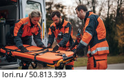 Emergency medical team transporting patient stretcher during outdoor operation in evening light. Стоковое AI-изображение, AI-художник Сергей Толмачёв / Фотобанк Лори
