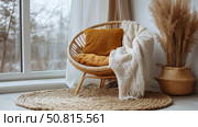 Cozy corner interior, round rattan chair with pillows and blanket, pampas grass, near window, for interior decoration. Стоковое AI-изображение, AI-художник Данила Большаков / Фотобанк Лори