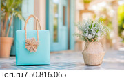 Summer Decor: Blue Bag with Raffia Accent and Wicker Vase with White Flowers on Tiled Floor. Стоковое AI-изображение, AI-художник Данила Большаков / Фотобанк Лори