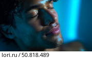Young man enjoys a moment of relaxation with soft blue lighting in a serene environment at night. Стоковое AI-изображение, AI-художник Сергей Толмачёв / Фотобанк Лори