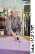 Attentive mature female dressmaker cutting textile using scissors in sewing workshop. Стоковое видео, видеограф Яков Филимонов / Фотобанк Лори