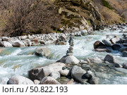 Ala-Archa Park, Fast flowing river with balanced rock cairn, rugged boulders, mossy hillside, bare trees, clear water, and untouched landscape ideal for mountaineering and backcountry exploration. Стоковое фото, фотограф Андрей Ка / Фотобанк Лори