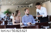 Couple resting, sitting in restaurant and ordering food. Waiter guy tells young women visitors of cafe about dish from chef. Стоковое видео, видеограф Яков Филимонов / Фотобанк Лори