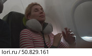 Woman in airplane seat, puts on neck pillow, gets comfortable and closes eyes for sleep during flight, close up of passenger relaxing in aircraft cabin, in-flight rest and travel comfort moment. Стоковое видео, видеограф Сергей Тимофеев / Фотобанк Лори