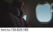 Woman sitting by airplane window with neck pillow, waking up and smiling, opens window shade to look at blue sky during flight, closeup passenger travel lifestyle and comfort, cabin interior view. Стоковое видео, видеограф Сергей Тимофеев / Фотобанк Лори