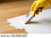 A man's hand in a rubber glove uses a large brush to apply white paint to a wooden floor. Стоковое AI-изображение, AI-художник Галина Эмберг / Фотобанк Лори