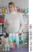 Interested pregnant woman in white sweater browsing store shelves, thoughtfully selecting household products while shopping for home essentials. Стоковое видео, видеограф Яков Филимонов / Фотобанк Лори