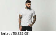 Attractive brutal tattooed bearded guy poses in black jeans and blank white t-shirt from premium thin summer cotton, isolated on white mockup. Стоковое AI-видео, аниматор Sergey Grishin / Фотобанк Лори