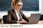 A female teacher works on a laptop, fills in an electronic diary. In the classroom, in the background of the blackboard. Стоковое AI-изображение, AI-художник Ирина Гильмуллина / Фотобанк Лори