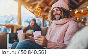Winter Getaway Game Night: A cheerful man with cards enjoying a cozy evening with friends near a snowscape, celebrating time together. Стоковое AI-изображение, AI-художник Данила Большаков / Фотобанк Лори