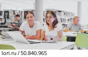 Two young women laughing and speaking loudly while using laptop in the library. Стоковое видео, видеограф Яков Филимонов / Фотобанк Лори