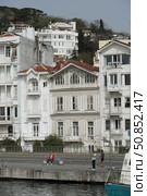 Istanbul, Turkey - Apr 01 2024: Traditional Ottoman-style wooden mansions along the Bosphorus waterfront in Istanbul, with people fishing and relaxing on the pier. Редакционное фото, фотограф Софья Соломонова / Фотобанк Лори