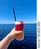 A bright cocktail in a woman's hand against a background of deep blue sea and clear sky. The atmosphere of summer relaxation and freedom. A trip on the water. Boat tour. Vacation on a yacht. Стоковое фото, фотограф Анна Чижова / Фотобанк Лори
