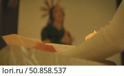 Woman reading Bible by candlelight in church with Virgin Mary on background. Стоковое видео, видеограф Igor Tichonow / Фотобанк Лори
